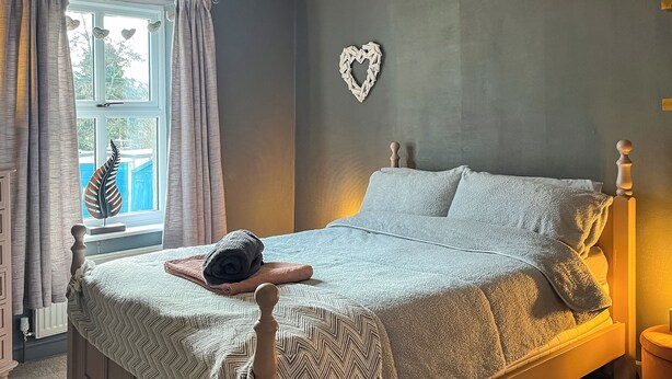 A bed with a patterned blanket, a heart-shaped wall decoration, and a window with curtains. - 1 bedroom accommodation in Kelbrook (Kelbrook)