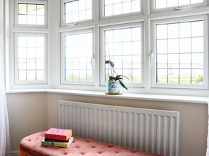 Une pièce avec un bow-window, un radiateur et une pile de livres posée sur un banc.