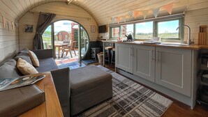 A cozy interior with a sofa, a small table, a kitchen area with a window, and a view of the outdoors. - Chesnut Pod - UK51519 (Newton Stewart)