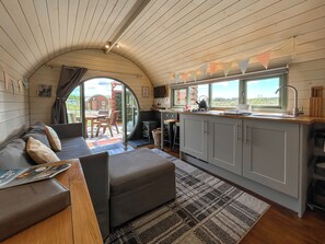 A cozy interior with a sofa, a small table, a kitchen area with a window, and a view of the outdoors. - Chesnut Pod - UK51519 (Newton Stewart)