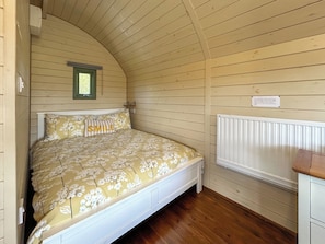 Un lit simple avec une literie à motifs floraux, une petite fenêtre et un radiateur blanc.