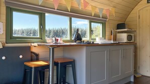 A kitchen with a wooden countertop, two bar stools, a microwave, and a view of trees through the windows. - Chesnut Pod - UK51519 (Newton Stewart)