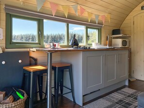 A kitchen with a wooden countertop, two bar stools, a microwave, and a view of trees through the windows. - Chesnut Pod - UK51519 (Newton Stewart)