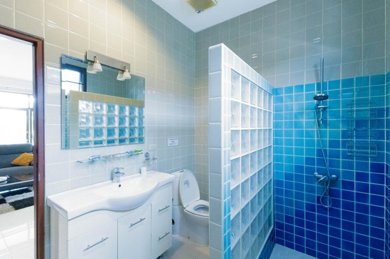 A modern bathroom with a white sink, toilet, and blue-tiled shower area.