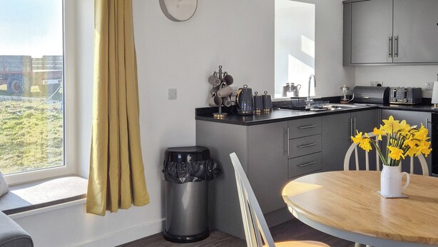A modern kitchen with grey cabinets, a sink, and a window with curtains. - Waking up to the wonderful views of the wide beaches and open skies. (North Uist)