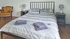 A neatly made bed with a grey and white striped duvet, two folded towels, a wooden chair, and two bedside tables with lamps. - Waking up to the wonderful views of the wide beaches and open skies. (North Uist)