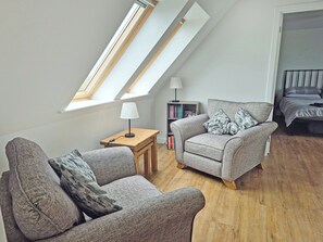 A loft bedroom with a skylight, a sofa, a side table, a lamp, a bookshelf, and a bed. - Waking up to the wonderful views of the wide beaches and open skies. (North Uist)