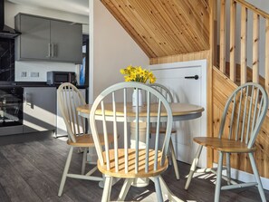 A modern kitchen with built-in appliances, a dining area with a round table and four chairs, and a wooden staircase.