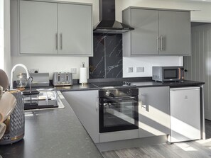 A modern kitchen with grey cabinets, a built-in oven, a microwave, and a marble backsplash. - Waking up to the wonderful views of the wide beaches and open skies. (North Uist)