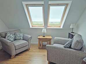 Una habitación con dos sofás grises, una pequeña mesa de madera y una lámpara. Hay tragaluces sobre los sofás.