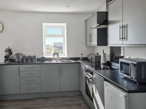 Una cocina moderna con armarios grises, horno empotrado, microondas y ventana con vistas al exterior.