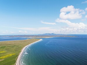 Vista aérea de un paisaje costero con playa, campos verdes y cielo azul despejado.