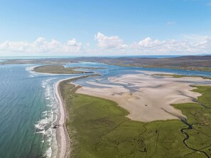 An aerial view of a coastal landscape with a beach, green fields, and a river.
