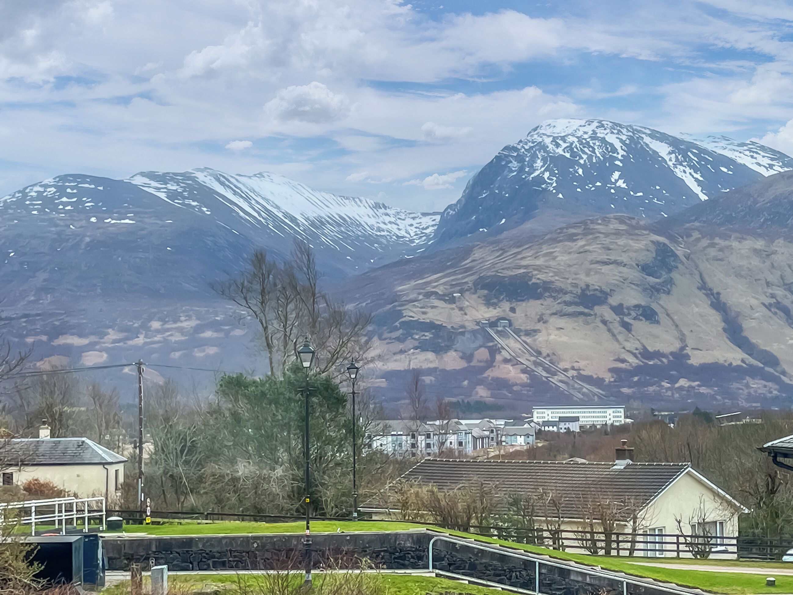 A mountain landscape with snow-capped peaks, a train track, and a small building with a white facade.