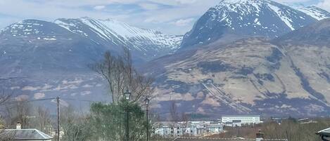 A mountain landscape with snow-capped peaks, a train track, and a small building with a white facade.