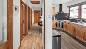 A modern kitchen with wooden cabinets, a stainless steel range, and a large window. - Flat 7, Canalside Apartments (Banavie, Fort William)