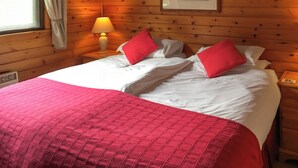A wooden cabin room with a bed, a nightstand, a lamp, and a framed picture on the wall. - The openness of the park and the closeness to the shore. (Acharacle, near Ardnamurchan)