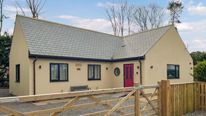 Une maison de plain-pied avec une porte rouge, un petit porche et une allée gravillonnée.