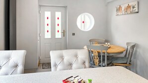 Un espace repas comprenant une table, des chaises, une porte blanche avec des panneaux de verre et un grand miroir rond fixé au mur.