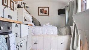 A compact room with a bed, a small kitchenette, a mounted TV, and a ceiling light fixture. - 1 bedroom accommodation in Ilfracombe (Ilfracombe)