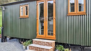 A green mobile home with a wooden door and windows, a brick entrance, and a gravel driveway. - 1 bedroom accommodation in Ilfracombe (Ilfracombe)
