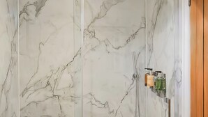 A bathroom with marble walls, a glass shower enclosure, and a wooden door. - 1 bedroom accommodation in Ilfracombe (Ilfracombe)