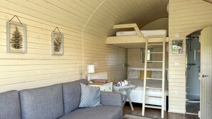 Ein gemütliches Zimmer mit grauem Sofa, einem kleinen Tisch mit Lampe, einem Etagenbett und einem Duschbereich.