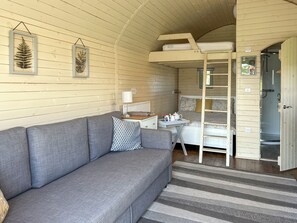A cozy room with a grey sofa, a small table with a lamp, a bunk bed, and a shower area. - Spruce Pod - UK51539 (Newton Stewart)