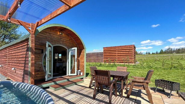 Eine Holzhütte mit Terrasse, Whirlpool und Blick auf ein Feld.