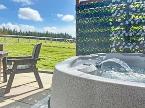Un jacuzzi con agua corriendo, una silla de madera y un área exterior con césped, una valla y árboles al fondo.