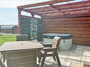 A wooden pergola with string lights, a hot tub, and a table with chairs in a garden setting. - Spruce Pod - UK51539 (Newton Stewart)
