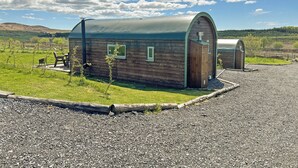 A rustic wooden cabin with a curved roof, a small porch with a bench, and a gravel driveway. - 1 bedroom accommodation in Newton Stewart (Newton Stewart)