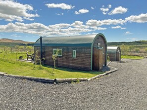A rustic wooden cabin with a curved roof, a small porch with a bench, and a gravel driveway. - 1 bedroom accommodation in Newton Stewart (Newton Stewart)
