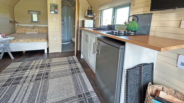 A compact room with a bed, a kitchenette, a shower, and a small window. - 1 bedroom accommodation in Newton Stewart (Newton Stewart)