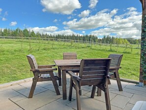 Un patio al aire libre con una mesa y sillas de madera, vistas a un campo cubierto de césped y un cielo despejado.