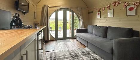 Un intérieur chaleureux avec un comptoir de cuisine, un canapé gris et une grande porte cintrée donnant sur l’extérieur.