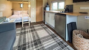Ein kleiner, gut beleuchteter Raum mit Etagenbett, Küchenzeile und Fernseher.