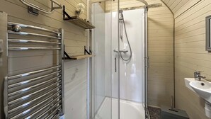 Eine Dusche mit Glastür, ein Metallhandtuchhalter und ein Waschbecken mit Spiegel.