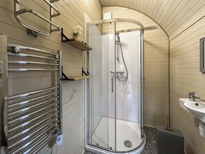 Una ducha con puerta de vidrio, un perchero metálico y un lavabo con espejo.