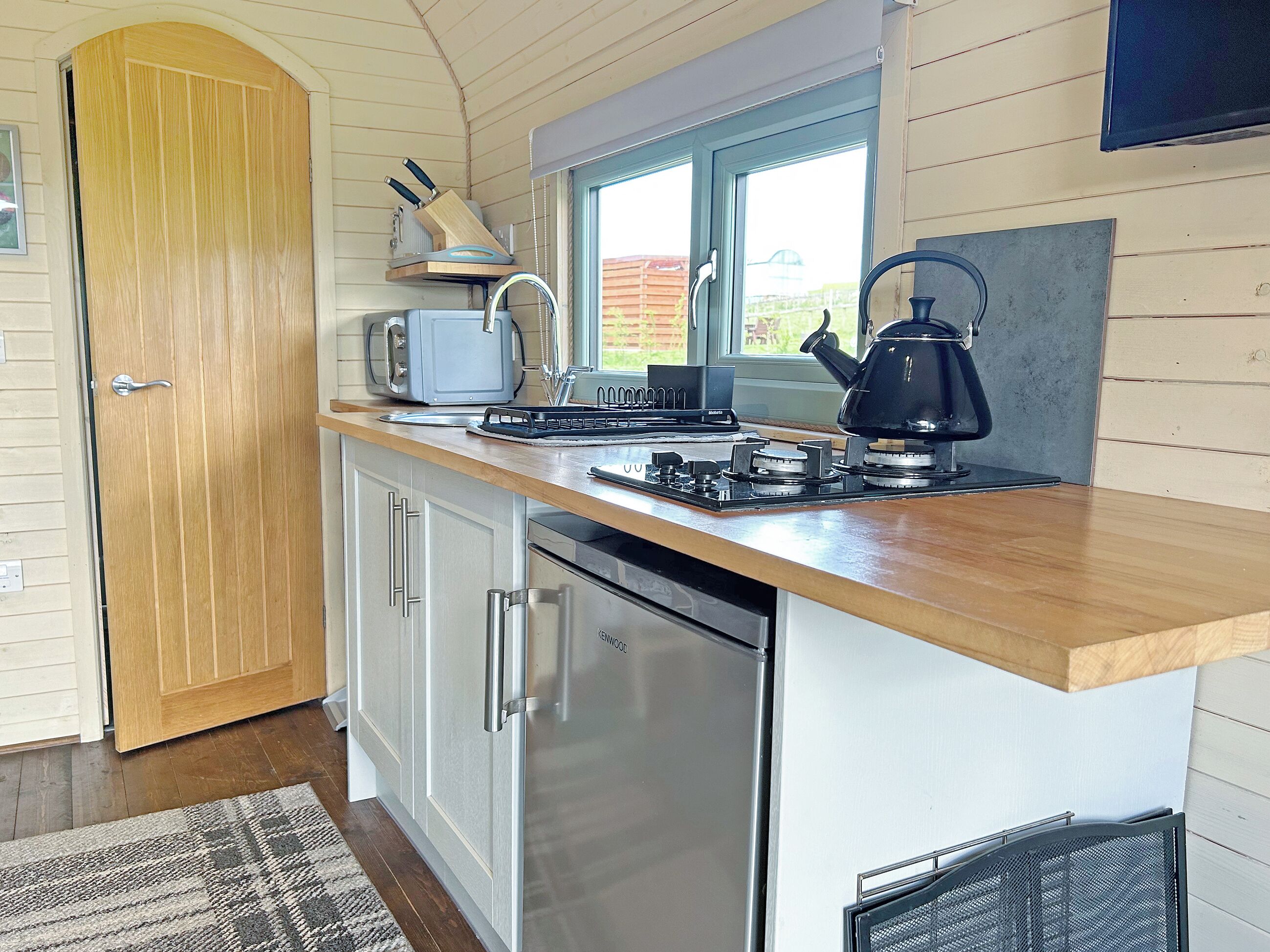 Una cocina compacta con encimera de madera, horno empotrado, refrigerador y ventana que proporciona luz natural.