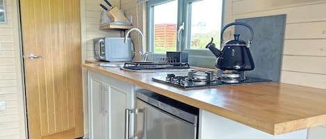 Une cuisine compacte dotée d’un plan de travail en bois, d’un four encastré, d’un réfrigérateur et d’une fenêtre laissant entrer la lumière naturelle.