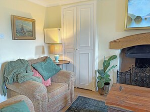 A cozy living room with a sofa, a small table with a lamp, a fireplace, and a framed painting on the wall.
