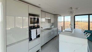 Cozinha moderna com forno embutido, micro-ondas e pia, com grandes janelas que proporcionam vista para o campo.
