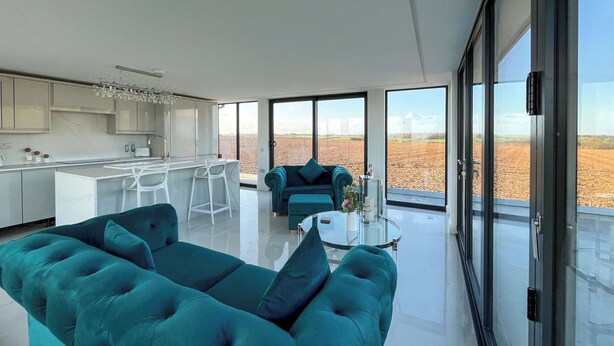 Uma sala de estar moderna com um sofá verde-água, uma mesa de centro de vidro e uma área de cozinha com armários brancos e um balcão.