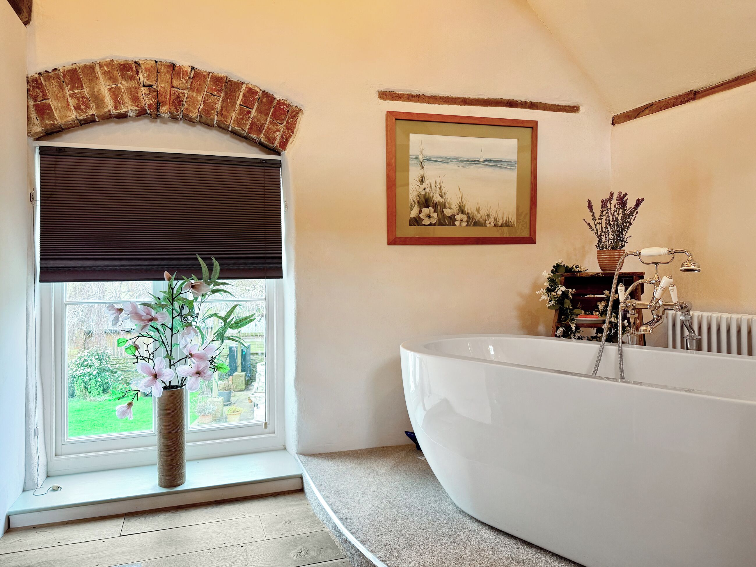 Un bagno con una vasca, una finestra vista, un quadro appeso al muro e una pianta in vaso.