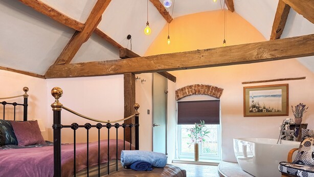 A bedroom with a four-poster bed, a wooden bench, a white bathtub, and a painting on the wall. - 1 bedroom accommodation in Blunsdon (Blunsdon)