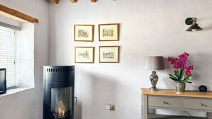 A room with a wood-burning stove, framed pictures on the wall, a lamp, and a vase with flowers. - 1 bedroom accommodation in Blunsdon (Blunsdon)
