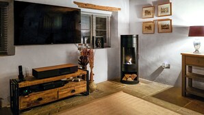 A living room with a TV, fireplace, wooden furniture, and framed pictures on the wall. - 1 bedroom accommodation in Blunsdon (Blunsdon)