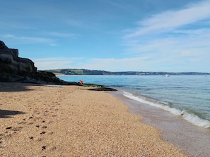 Ein Kiesstrand mit einer felsigen Klippe und ruhiger See.