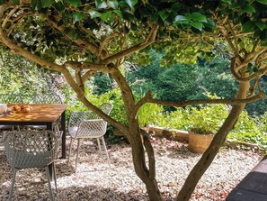 An outdoor seating area with a table and chairs under a tree, surrounded by greenery. - 3 bedroom accommodation in Kingsbrisge (Kingsbrisge)